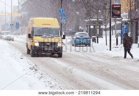 Karlstad Sweden - January 30 2014: A yellow DHL parcel delivery van driving on the street Ostra Torgatan with winter road conditions in the city center during a snowfall.