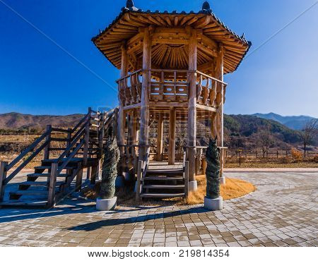 Two bronze statues of dragons standing in front of a two story wooden gazebo in a public park located near Geumsan, South Korea