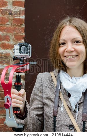 The girl smiles and holds in the hand an action camera on the gimbal stabilizer on the street of Etretat, France, September, 30, 2014.