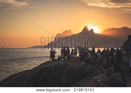 RIO DE JANEIRO BRAZIL - SEPTEMBER 23 2017: Many people sitting on Arpoador Stone to watch the sunset in a sunny afternoon with clouds. Rio de Janeiro Brazil.