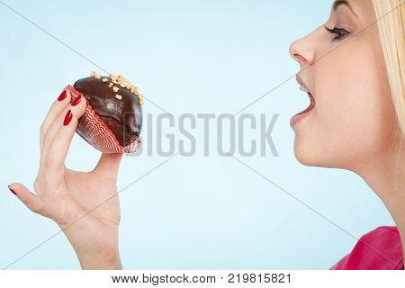 Diet sweets food concept. Woman holding delicious chocolate cupcake with peanut frosting about to take bite