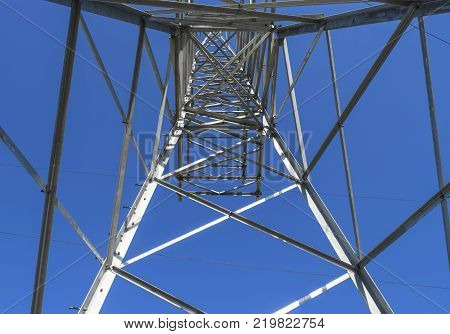Supports high-voltage power lines against the blue sky. View from the bottom up.