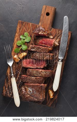 Closeup ready to eat steak new York beef breeds of black Angus with herbs, garlic and butter on a wooden Board. The finished dish for dinner on a dark stone background. Top view.