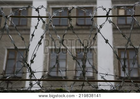 Barbed wire barrier with beautiful sky clouds and brick building behind the scene.