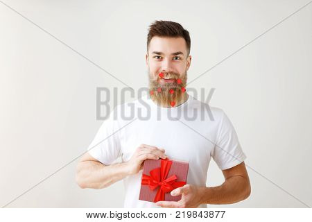 Horizontal shot of cheerful bearded male with trendy hairdo, holds gift box, prepares surprise for girlfriend or friends, isolated over white background. People, holidays and presents concept.