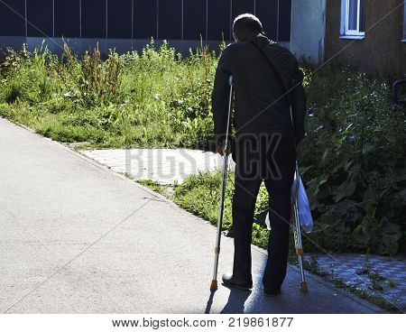 An elderly man strolling through the Park on crutches.