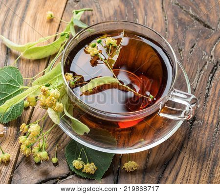 Cup of linden tea and lime flowers on the wooden table.