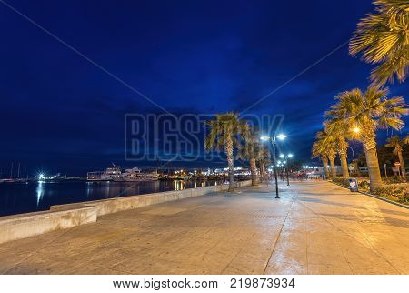 View over the seafront of the city Paphos in Cyrpus. Palm silhouettes, boats in the water and golden sunset over the sea with dramatic cloudy sky.