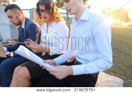 Young contemporary confident people, two boys and two girls, perspective entrepreneurs, students smiling, chatting with each other, using gadgets, laptops, tablet and smartphone for work with office programs, drawing up business plan, discuss working mome
