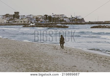 Coastal landscape with the beach of Forio, Ischia sland tourist resort of Naples bay Italy, dog and her master stroll on Forio beach, beach without tourists for cloudy sky