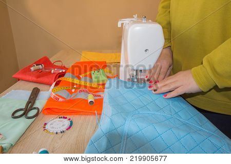 people needlework sewing and tailoring concept - tailor woman with thread in needle stitching fabric pieces together. Clothes designer at work in her office. Garment industry tailoring concept
