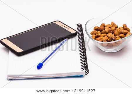 mobile phone and notebook on the desk with bowl of huzelnuts for keeping energy while working