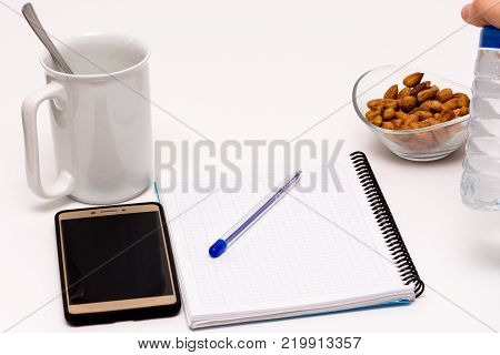 mobile phone and notebook on the desk with bowl of huzelnuts and the cup of coffee for keeping energy while working