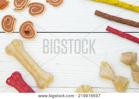 Pet care, veterinary concept. Delicious snacks for a pet. A white wooden background with a frame of dog snacks- chewing bones, twisted snacks and crunchy sticks.Space for your text or product display.