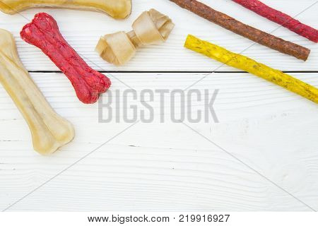 Pet care, veterinary concept. Delicious snacks for a pet. A white wooden background with dog snacks - chewy bones and chrunchy sticks of different colors .Space for your text or product display.
