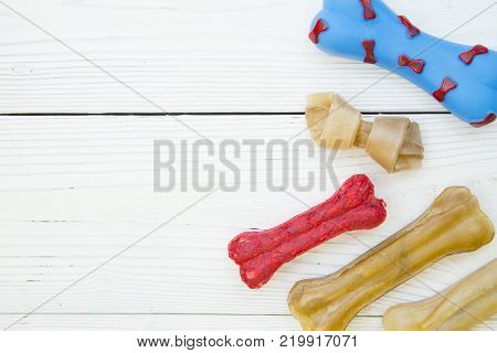 Pet care, veterinary, concept. Delicious snacks for a pet. A white wooden background with bones for dogs- chewy snacks and a rubber toy .Space for your text or product display.