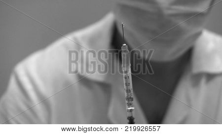 doctor in mask with syringe in hand preparing for the shot.