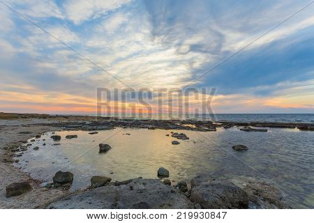View over the seafront of the city Paphos in Cyrpus. Palm silhouettes, boats in the water and golden sunset over the sea with dramatic cloudy sky.