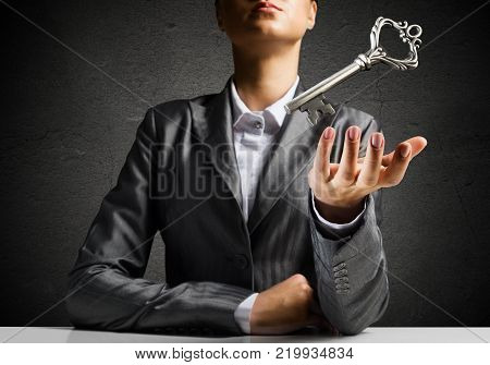 Cropped image of businessman in suit keeping big key in hand with dark wall on background.