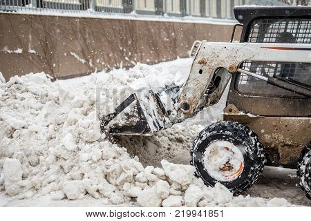 Small tractor loader machine clean  and load snow and ice into a truck from a city streets after heavy snowfall