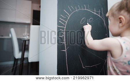 Cute little girl drawing on blackboard. Toddler girl having fun outdoors, holding chalk and drawing.