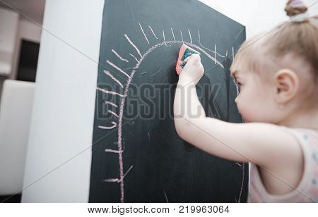 Cute little girl drawing on blackboard. Toddler girl having fun outdoors, holding chalk and drawing.