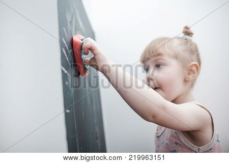 Cute little girl drawing on blackboard. Toddler girl having fun outdoors, holding chalk and drawing.