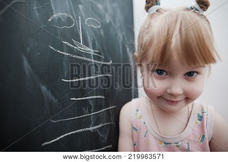 Cute little girl drawing on blackboard. Toddler girl having fun outdoors, holding chalk and drawing.