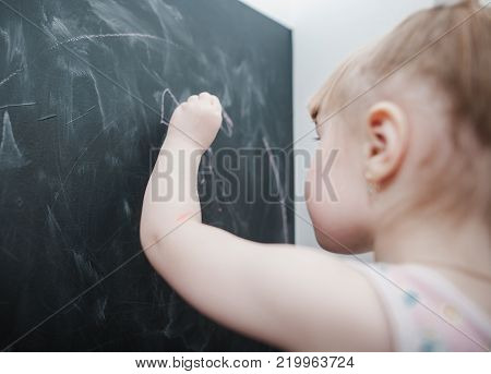 Cute little girl drawing on blackboard. Toddler girl having fun outdoors, holding chalk and drawing.
