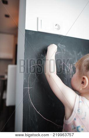 Cute little girl drawing on blackboard. Toddler girl having fun outdoors, holding chalk and drawing.