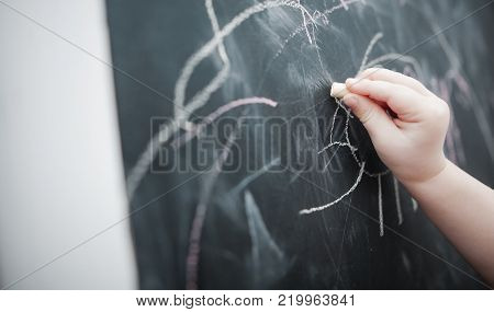 Cute little girl drawing on blackboard. Toddler girl having fun outdoors, holding chalk and drawing.