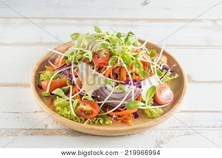 Healthy vegan lunch dish.Tomato, cucumber, red cabbage, carrot, onion and micro greens vegetables salad on wooden plate.