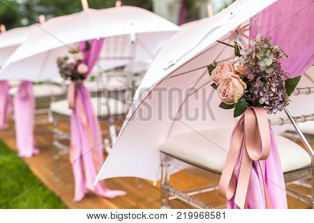Chairs, flowers and umbrellas at an outdoor ceremony.