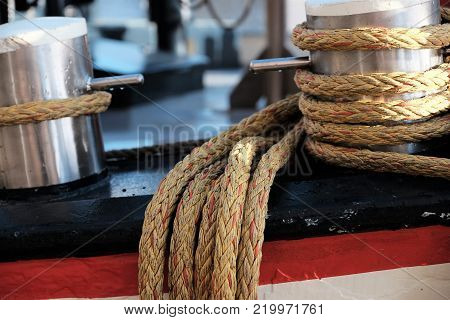 Braided ropes tied to steel bollards on deck of a docked tall ship.