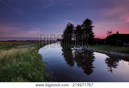 A docked motorboat and a farmhouse at a small river at dawn in a rural region near Zuidlaren, the Netherlands.