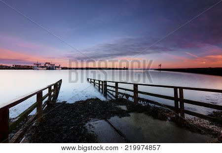 Looking across a slipway in the center towards two ferries waiting in a cove in a calm sea under a blue and orange dawn