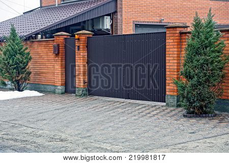 part of a brick fence with closed door and decorative pine trees on the street