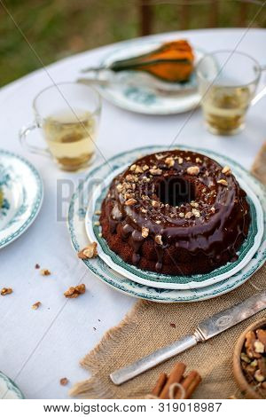 Chocolate Bundt Cake With Chocolate Glaze And Nuts On Top On Vintage Plates On Table With Grey Table