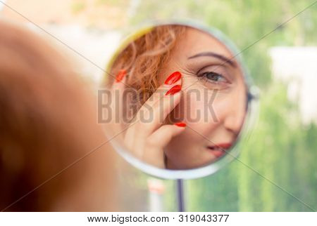 Reflection In The Mirror. A Woman Looks In The Mirror Noticing The First Wrinkles, Signs Of Aging. A