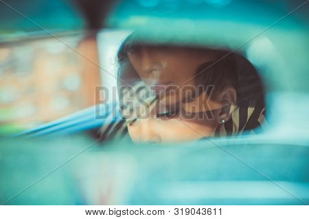 Beautiful Woman Driver Reflecting In The Rearview Mirror. Driving Her Car Concept. Artistic Shot Wit