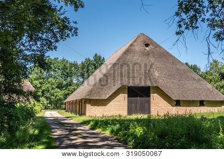 Bokrijk, Belgium - June 27, 2019: Giant Barn With Gray Straw Roof Is Set In Green Of Meadow And Surr