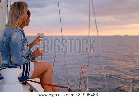 Two Joyful Women Are Celebraiting Good Summer Day At The Yacht While Watching Beautiful Sunset.