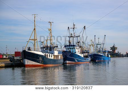Three Blue Fishing Boats At The Quay In The Port Of Buesum On The North Sea In Germany Against The B