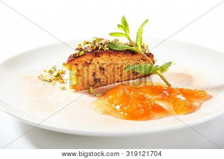 Healthy nut cake with apricot jam isolated on white background. Slice of walnut carrot sponge cake decorated with pistachios and fruit confiture on white round plate for restaurant menu