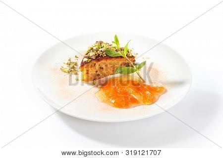 Healthy nut cake with apricot jam isolated on white background. Slice of walnut carrot sponge cake decorated with pistachios and fruit confiture on white round plate for restaurant menu