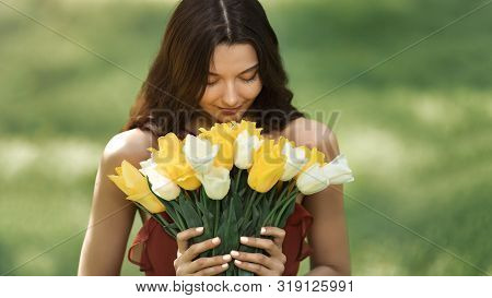 Attractive Woman In Red Dress With A Bouquet Of Spring Flowers Against Nature Bokeh Green Background