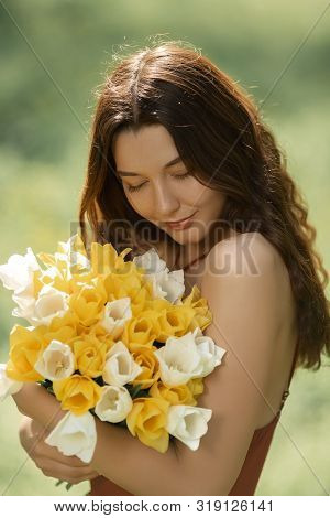Attractive Woman In Red Dress With A Bouquet Of Spring Flowers Against Nature Bokeh Green Background