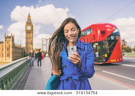 Asian woman using phone walking in London city urban lifestyle. Businesswoman portrait smiling happy holding cellphone in autumn outdoor.