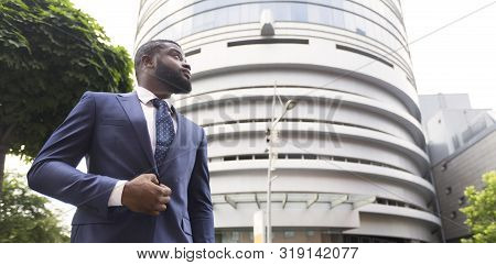 Portrait Of Thougtful Confident Black Businessman Against Modern Office Center Background, Low-angle
