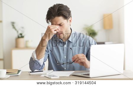 Eyes Fatigue. Tired Man Massaging His Nosebridge Holding Glasses Sitting At Laptop In Office